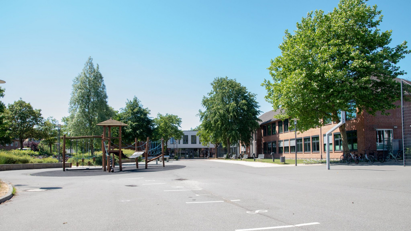 Schulhof der Eider Trenne Schule Tönning mit Bäumen, Klettergerüst und dem Schulgebäude im Hintergrund